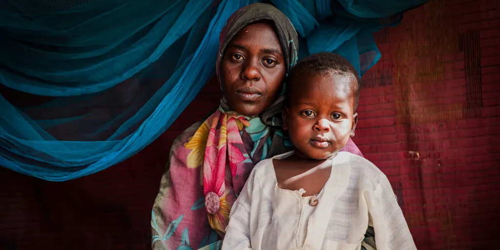A Sudanese mother and child sit together, looking at the camera.