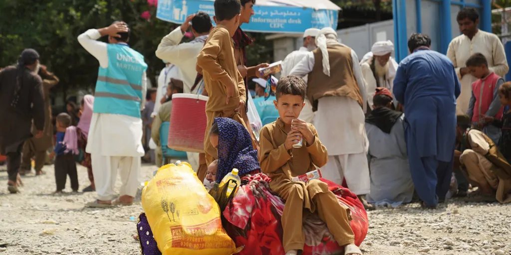 Afghan boy sits on bags at Torkham border crossing as families returning from Pakistan receive assistance from UNHCR.