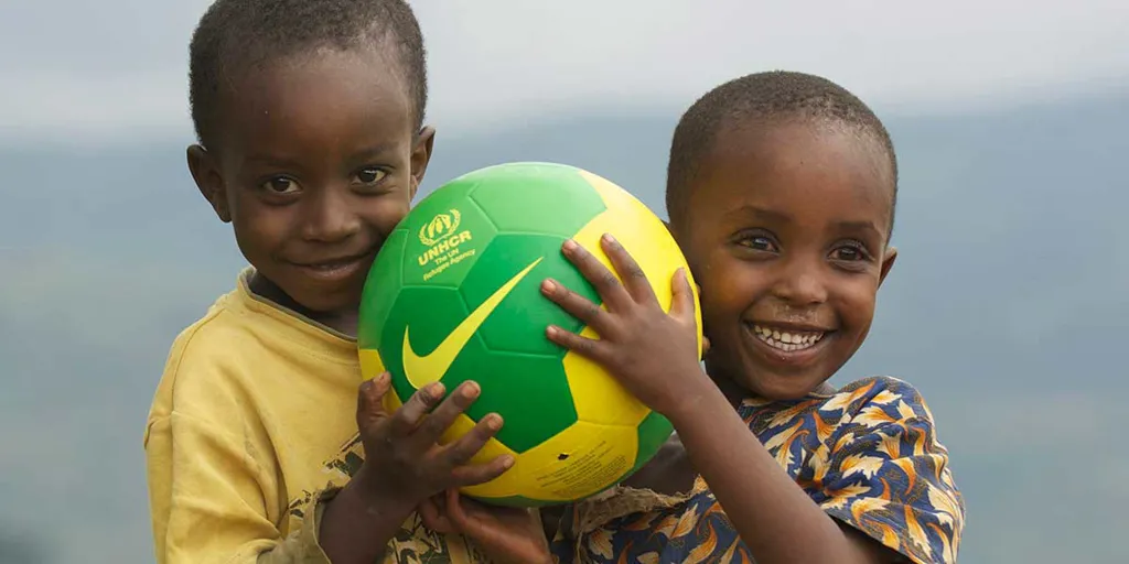 Two young children hug a soccer ball, smiling.